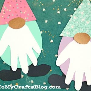 Two Easter egg gnome crafts made from colorful craft foam, with polka dot and floral hats, white handprint beards, and oval noses are displayed on a green star-patterned background—perfect as a cheerful handprint spring gnome project.