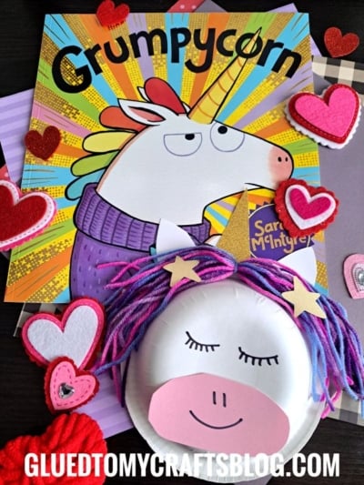 A colorful book titled Grumpycorn with a grumpy unicorn on the cover is surrounded by felt hearts and a unicorn face craft made from yarn, paper, and a paper bowl unicorn. The website gluedtomycraftsblog.com is visible.