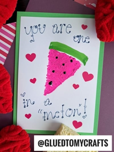 A handmade card featuring a sponge painted watermelon slice, surrounded by red heart stickers. “You are one in a melon!” is written in decorative handwriting, with the Instagram handle @GLUEDTOMYCRAFTS at the bottom.