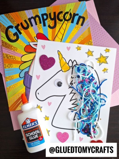 A fun unicorn mane craft for kids with a coloring page, yarn unicorn hair, googly eye, glittery heart stickers, Elmer’s glue, and the book “Grumpycorn” on a pink polka-dot background. Text: @GLUEDTOMYCRAFTS.