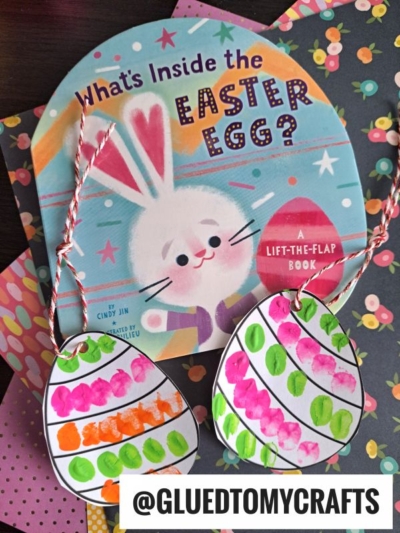 A colorful children’s book titled What’s Inside the Easter Egg? featuring a bunny is shown with two hand-painted thumbprint easter egg crafts on strings, all placed on patterned paper backgrounds.
