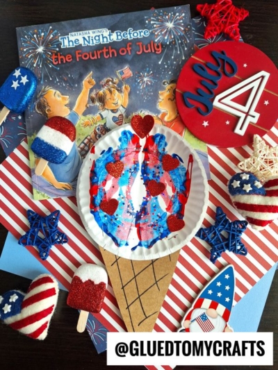A festive Fourth of July craft scene with a paint splat ice cream cone decorated in red, white, and blue, surrounded by patriotic decorations, felt hearts, star shapes, and the book The Night Before the Fourth of July in the background.