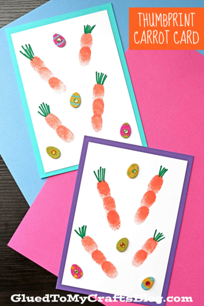 Two handmade thumbprint carrot cards with orange designs and green paper stems, each adorned with small, colorful, glittery egg stickers, are displayed on bright pink and blue papers.