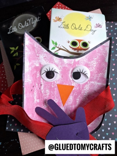 A handmade pink owl craft with big googly eyes, orange beak, and purple wings—perfect as a Mother's Day keepsake—sits in front of two children’s books, “Little Owls Night” and “Little Owls Day,” against heart-patterned paper.