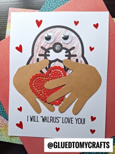 A handmade Valentine’s card featuring a walrus face with googly eyes, paper hands holding a red heart doily, small red hearts—perfect as a Mother's Day keepsake—with the cute text “I will ‘walrus’ love you!” on the bottom.
