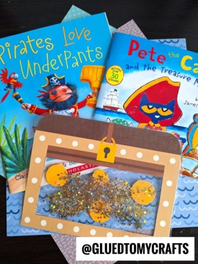 Two colorful children's books, Pirates Love Underpants and Pete the Cat and the Treasure Map, sit on patterned paper with a pirate-themed shaker craft and a stained glass treasure chest featuring gold glitter and coins. @GLUEDTOMYCRAFTS appears at the bottom.