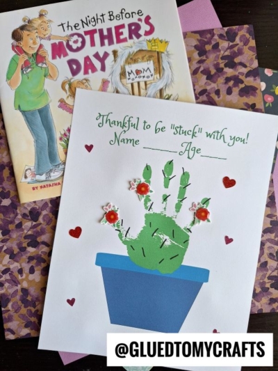 A Mother’s Day cactus handprint craft with “Thankful to be stuck with you! Name ____ Age ____” written on it, decorated with hearts and flower stickers, sits beside a special Mothers Day book.