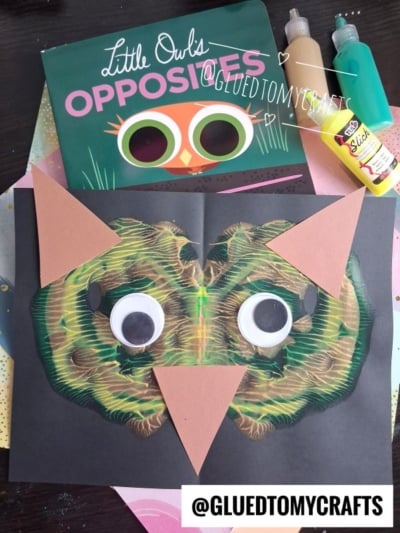 Children’s owl craft featuring a paint splat owl face with brown paper triangles and googly eyes on black paper, surrounded by paint bottles, the book “Little Owl’s Opposites,” and the text “@GLUEDTOMYCRAFTS” at the bottom.
