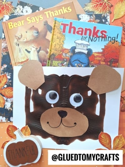 Children’s books on gratitude, autumnal crafts, and a brown bear face made from a playful paint splat teddy bear technique on paper, set against a white sheet. Surrounded by fall leaves, a Thankful pumpkin, and finished with the @GLUEDTOMYCRAFTS tag at the bottom.
