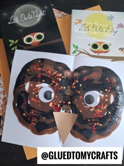 Children’s paint splat owl face craft made of brown paint, googly eyes, star-shaped glitter, and a paper beak, surrounded by owl-themed books. The handle @gluedtomycrafts appears at the bottom.