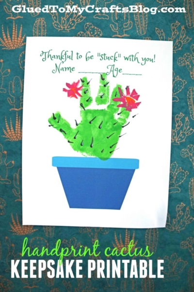 A cactus handprint craft with red paper flowers in a blue pot on white paper. The text reads, Thankful to be stuck with you! Name ___ Age ___. The background features a teal cactus pattern—a perfect cactus handprint Valentine’s project.