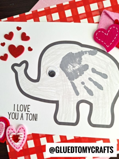 A gray elephant outline with a child’s handprint as its ear, googly eye, and red felt hearts, perfect for celebrating National Grandparent’s Day. Text reads I LOVE YOU A TON! Felt hearts and a checkered pattern are in the background. @GLUEDTOMYCRAFTS at the bottom.