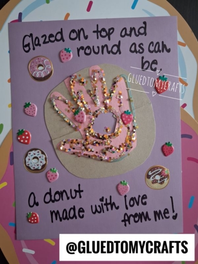 Handmade card with a handprint painted pink and decorated with glitter and donut stickers. Perfect for celebrating National Grandparent’s Day, the text reads: Glazed on top and round as can be, a donut made with love from me! @GLUEDTOMYCRAFTS at the bottom.