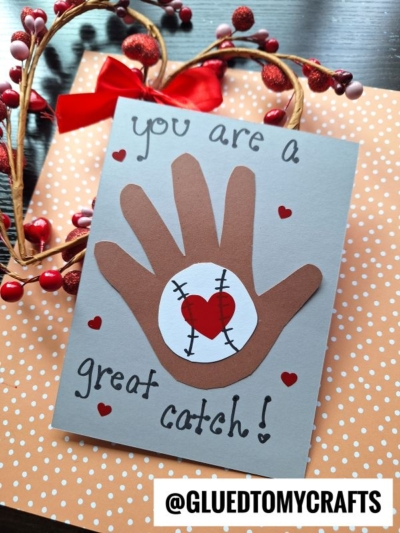 Handmade card with a brown paper hand, a baseball with a red heart in the palm, small red hearts, and the text “You are a great catch!” on a gray card. Perfect for celebrating National Grandparent’s Day, this thoughtful design features decorative berries and polka dot paper in the background.