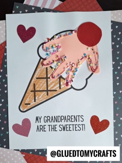 A handmade card with an ice cream cone and a pink handprint as the ice cream, decorated with colorful sprinkles, hearts, and the text “My grandparents are the sweetest!”—perfect for celebrating National Grandparent’s Day.