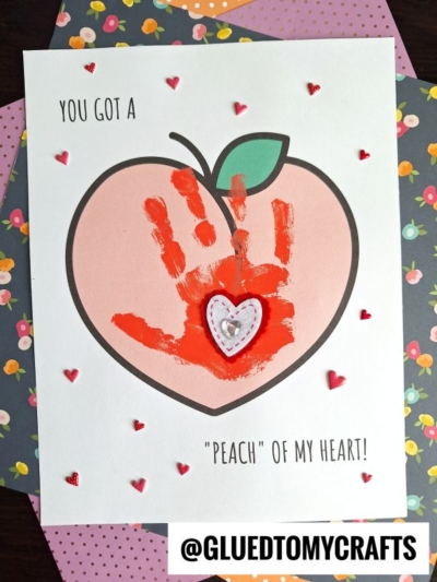 A handprint craft for National Grandparent’s Day features a peach drawing with an orange handprint inside, heart stickers, and the phrase “You got a peach of my heart!” on decorated paper.