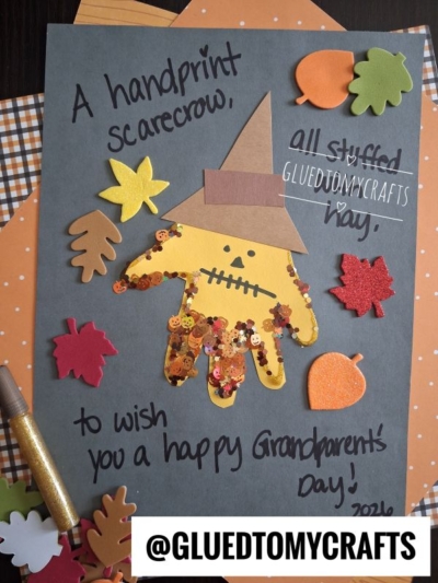 A handmade card featuring a scarecrow made from a yellow handprint, decorated with a hat, sequins, and surrounded by paper leaves. The card wishes a happy National Grandparent’s Day to celebrate your special grandparents.