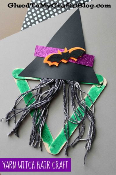 A Yarn witch craft made from green popsicle sticks, black yarn for hair, and a paper witch hat with a purple glitter band and orange bat. Text reads, Yarn Witch Hair Craft.