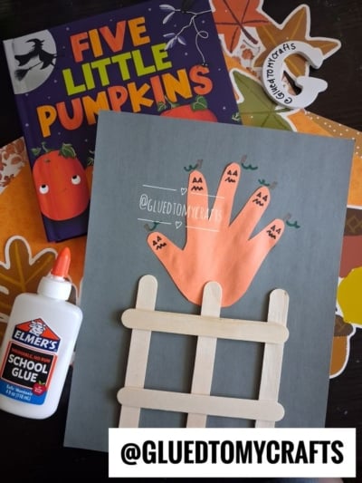 A craft featuring a handprint pumpkin design on top of a popsicle stick fence
