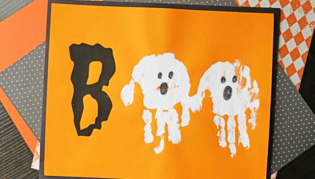 A Halloween-themed craft featuring a handprint boo ghost: the letter B cut from black paper and two white handprint ghosts forming "BOO" on orange paper, decorated with googly eyes and black marker details.