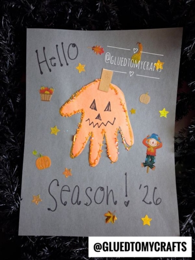 Gray paper with “Hello Season! ‘26” features a delightful pumpkin handprint craft, glitter, stickers of pumpkins, leaves, a cupcake, and a scarecrow—perfect inspiration for your fall keepsake ideas. Orange and yellow stars are scattered around. @GLUEDTOMYCRAFTS handle is shown.