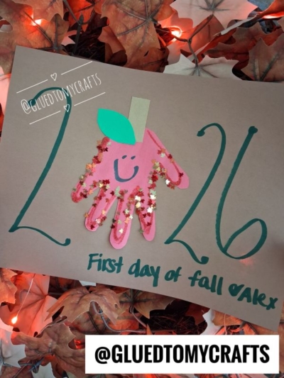 A craft featuring a handprint apple with a smiley face, labeled “First day of fall, Alex.” Large green numbers 26 are written amid autumn leaves and fairy lights—perfect inspiration for those searching for fall keepsake ideas. Instagram handle @GLUEDTOMYCRAFTS appears twice.