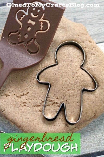 A gingerbread man cookie cutter and a spatula with a gingerbread man design rest on brown, gingerbread scented playdough. The text at the bottom reads gingerbread playdough.