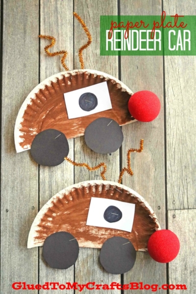 Two paper plate Rudolph cars shaped like reindeer, with brown plates, red pom-pom noses, black paper wheels, and pipe cleaner antlers, displayed on a wooden surface. Text reads paper plate reindeer car.