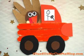 A popsicle stick Thanksgiving truck, painted red-orange, carries a brown paper turkey. Black wheels and a hand-drawn driver add charm, while gold stars decorate the festive background.