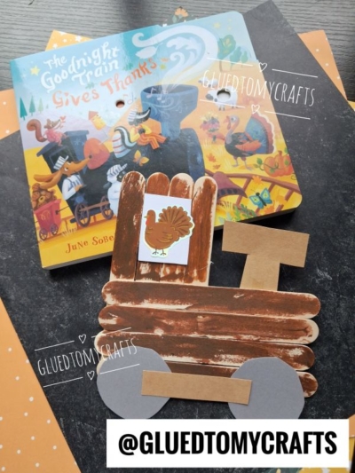 A children’s book titled The Goodnight Train Gives Thanks is next to a popsicle stick Christmas train craft with brown painted sticks, gray wheels, and a paper turkey. @GLUEDTOMYCRAFTS is written on the image.