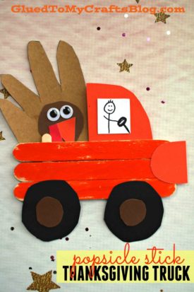 A popsicle stick Thanksgiving truck, painted red-orange, carries a brown paper turkey. Black wheels and a hand-drawn driver add charm, while gold stars decorate the festive background.