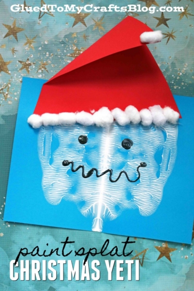A blue paper features a paint splat yeti face with googly eyes, a red paper Santa hat, cotton ball trim, and a curly black mouth. Star patterns fill the background. Text reads: paint splat CHRISTMAS YETI.