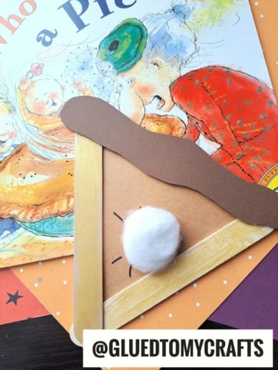 A children’s pie-themed craft made from paper and a cotton ball as whipped cream, with a brown strip as crust—similar to a craft stick apple pie—placed over a book cover with illustrated characters. Username @GLUEDTOMYCRAFTS is displayed at the bottom.