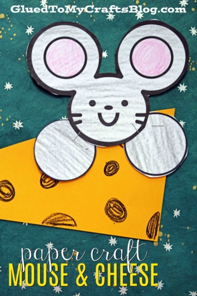 A handmade paper mouse and cheese craft features a smiling mouse with large ears in white and pink beside a yellow, holey cheese slice. The dark green background is dotted with stars. Text reads “paper craft mouse & cheese.”.