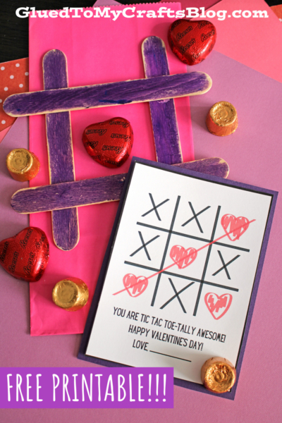 A Valentine’s Day-themed flat lay featuring a handmade popsicle stick tic tac toe board, chocolate hearts and candies, and a card reading “You are tic tac toe-tally awesome! Happy Valentine’s Day! Love ___”. Text: “FREE PRINTABLE!!!”.