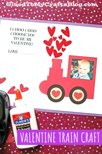 A Valentines Day craft features a paper valentine train with heart accents and a child's photo in the window, surrounded by red paper hearts, Elmer's glue, and a sweet message: I choo choo choose you to be my Valentine!.