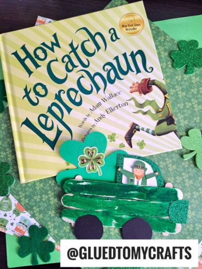 A St. Patrick’s Day craft scene featuring the book How to Catch a Leprechaun, green shamrock decorations, and a popsicle stick leprechaun truck with a leprechaun image, all arranged on patterned paper.