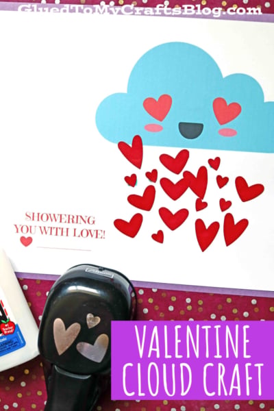A paper valentine cloud craft featuring a smiling blue cloud with red and pink hearts raining down, plus the text SHOWERING YOU WITH LOVE! and VALENTINE CLOUD CRAFT. Glue, a heart-shaped punch, and scissors are nearby.