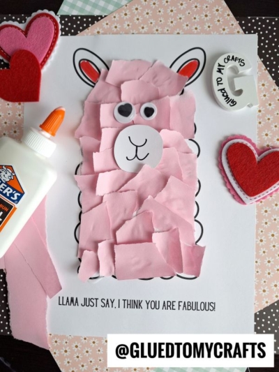 A Torn Paper Llama craft made with pink paper pieces, googly eyes, and a hand-drawn face on white paper. Felt hearts, a bottle of glue, and a round Glued to My Crafts badge surround this adorable project.