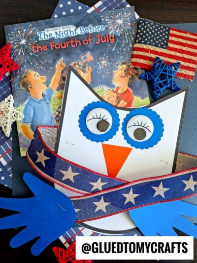 A blue handprint owl hug craft with googly eyes, a star-patterned ribbon, and patriotic decorations sits atop a children’s book titled The Night Before the Fourth of July.