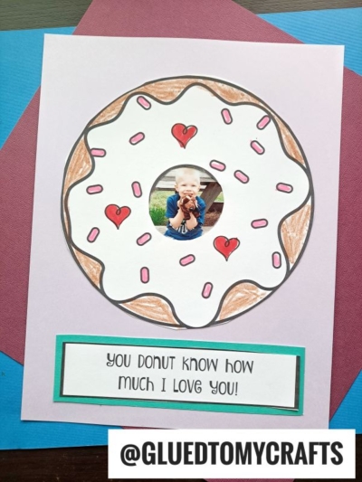 A handmade card showcases a donut love frame with white icing, red hearts, and pink sprinkles. In the donut’s center is a photo of a smiling child. Below, the sweet message reads: You donut know how much I love you!.