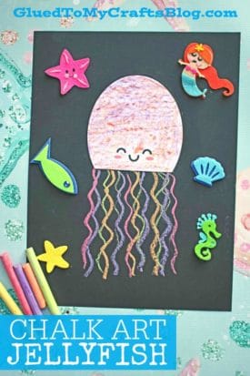 A chalk art jellyfish with a pink head and colorful wavy tentacles smiles on black paper, surrounded by foam sea-themed stickers and chalk pieces. Text at the bottom reads, CHALK ART JELLYFISH.