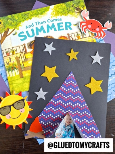 A children's summer-themed paper tent kid craft project with cut-out stars, a tent, a sun with sunglasses, and a red crab, placed on top of the book And Then Comes Summer. @GLUEDTOMYCRAFTS is written at the bottom.