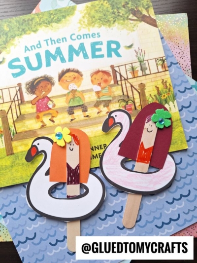 Two handmade popsicle stick pool float puppets with paper hair, drawn faces, and flamingo floaties rest on a children’s book titled “And Then Comes Summer.” Perfect as a pool float craft for kids. Instagram: @GLUEDTOMYCRAFTS.