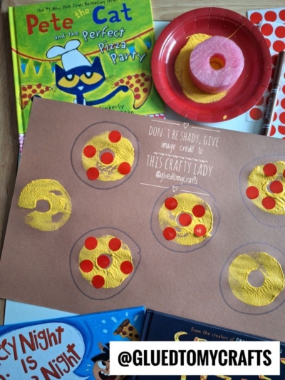 A children’s pizza craft made with yellow paint and red circles on brown paper is shown, surrounded by Pete the Cat books, a red plate, a sponge, pool noodle craft supplies, and a sheet of red dot stickers. @GLUEDTOMYCRAFTS is labeled at the bottom.