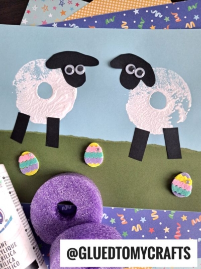 A kids’ pool noodle craft project shows two sheep made from painted foam ring prints, with black paper faces and legs, googly eyes, and three colorful foam Easter eggs on green and blue paper. Arts and crafts supplies are nearby.