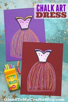 Two colorful paper chalk art dresses are drawn on purple and burgundy paper. A Crayola chalk box and pastel chalk pieces rest beside the drawings. The text reads “Chalk Art Dress.” The background features a blue and purple speckled surface.