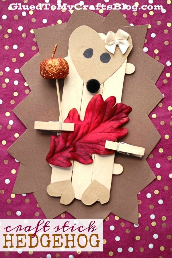 Children's craft project of a hedgehog puppet made from popsicle sticks, decorated with fall-themed materials.
