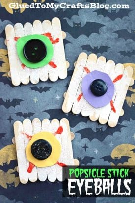 Three Halloween crafts made from popsicle sticks, foam circles, and buttons form spooky popsicle stick eyeball decorations, arranged on a bat-patterned background with the text POPSICLE STICK EYEBALLS at the bottom.
