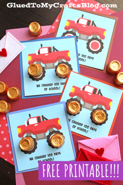 Three handmade cards featuring red monster trucks with gold-wrapped candies for wheels celebrate how we crushed 100 days of school! Displayed on a pink background with felt hearts and Rolo chocolates, this craft comes with a free printable.